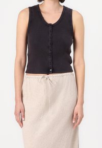 Donna che indossa un top nero a coste senza maniche con bottoni e una gonna beige con coulisse, vista dalle spalle alla vita.