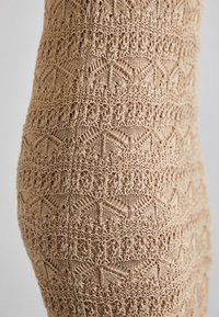 Tissu tricoté au crochet beige avec des motifs géométriques et floraux détaillés, montrant un design de dentelle ajourée et texturée.
