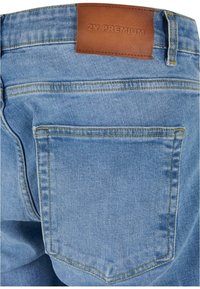 Jeans de mezclilla azul claro con una textura suave, que presentan una parche de cuero marrón etiquetado como "2Y PREMIUM" y costuras dobles a lo largo de los bolsillos.