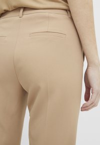 Beige op maat gemaakte broeken met een gladde textuur, voorzien van een achterzak en een strakke tailleband, gecombineerd met een lichtbruine top.