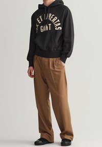 Černá mikina s kapucí a přední kapsou, doplněná světlými skládacími kalhotami a černými botami na slip. Jednoduchý a neformální design.