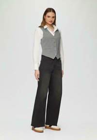 Grijze, getailleerde vest over een wit shirt, gecombineerd met losse zwarte jeans. Geaccentueerd met knopen, gestyled met platform schoenen. Eenvoudig, op maat gemaakt ontwerp.