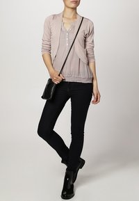 Ljusrosa cardigan med en texturerad, knappad topp, i kombination med mörka skinny jeans och svarta ankelboots. Utseendet kompletteras med en svart axelväska.