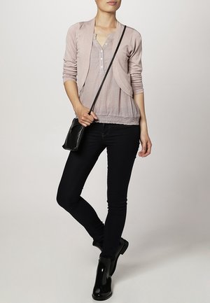 Cardigan rosa chiaro con una parte superiore testurizzata e bottoni, abbinato a jeans skinny scuri e stivali neri alla caviglia. L'outfit è completato da una borsa a tracolla nera.