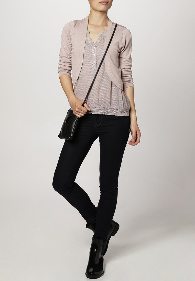 Ljusrosa cardigan med en texturerad, knappad topp, i kombination med mörka skinny jeans och svarta ankelboots. Utseendet kompletteras med en svart axelväska.