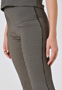 Leggings con motivo houndstooth nero e crema, con finitura testurizzata e dettagli in piping nero sui lati. La vista ravvicinata mostra la vestibilità e la qualità del tessuto.