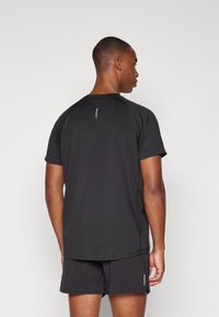 Schwarzes Sport-T-Shirt, kurze Ärmel, runder Halsauschnitt, nahtlose Schultern, kontrastierende Nähte, Logo-Detail auf dem Rücken. Getragen mit passenden Shorts.