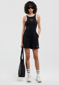 Mustas tank top valge äärisega, mustad lühikesed püksid, must kott, valged sneakers ja triibulised sokid. Kuurud juuksed ja päikeseprillid täiendavad välimust.