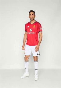 Sarkans Manchester United kreklis ar melniem akcentiem, baltas šortus un baltas zeķes. Kreklim ir apaļa apkakle un logo uz krūšu.