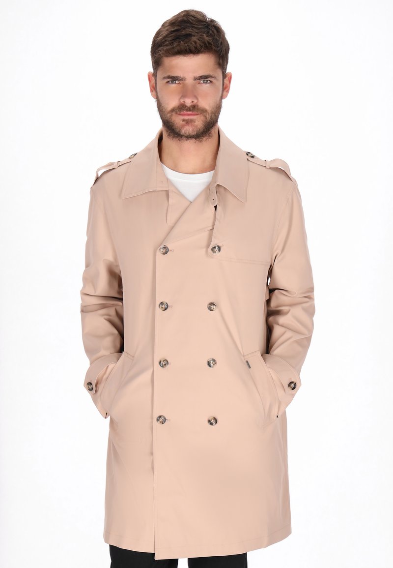 Trench beige doppiopetto con grandi bottoni, alamari sulle spalle e tasche laterali. Materiale liscio e impermeabile; design lungo fino al ginocchio.
