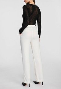 Czarny top z długim rękawem, wykonany z przezroczystego, teksturowanego materiału, zestawiony z kremowymi spodniami o szerokiej nogawce. Spodnie mają tylne kieszenie i gładkie wykończenie.