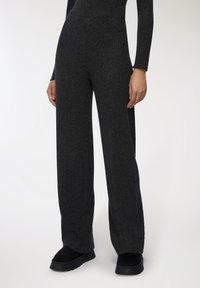 Ciemnoszare dzianinowe spodnie o fakturze prążkowanej, wysoki stan oraz szerokie nogawki, w połączeniu z czarnym obuwiem.