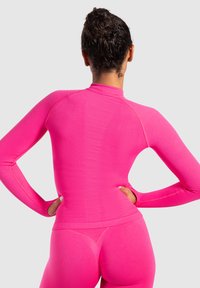Aansluitende lange mouwen top en legging in helder roze, gemaakt van glad, rekbaar materiaal met ribbelstructuur accenten langs de naden.