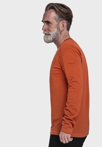 Langärmliges Hemd aus orangefarbenem Baumwollstoff, mit Rundhalsausschnitt und subtilen Nähdetails. Logo am linken Arm und taillierte Silhouette.