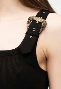 Μαύρο ριμπ αμάνικο τοπ με φαρδιά τιράντα που διαθέτει περίτεχνη αγκράφα Versace Jeans Couture σε χρυσαφί απόχρωση στον ώμο.