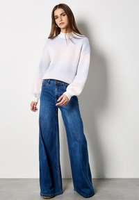 Witte geribde gebreide trui met hoge ronde hals en pofmouwen, gecombineerd met blauwe denim jeans met wijde pijpen.