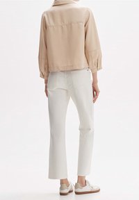 Lichtbeige cropped jack met opgezette mouwen, gecombineerd met witte rechtvaardige jeans. Het schoeisel bestaat uit witte sneakers met tan accenten.