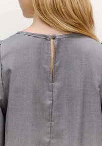 Graues Stoffkleidungsstück mit einem Schlüsselloch-Rücken, das einen stoffbezogenen Knopf am Hals und eine glatte, weiche Textur aufweist.