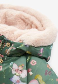 Chaqueta verde acolchada con ilustraciones de flores y hadas. Presenta un suave forro de piel sintética rosa y acentos de hardware dorado a lo largo del zipper.