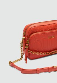 Rote, strukturierte Kunstleder-Crossbody-Tasche mit zwei Reißverschlussfächern, goldenen Kettenakzenten und verstellbarem Trageriemen. Mit geprägtem Logo-Detail.