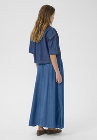 Blå denim cropped top med korte ærmer, parret med en lang, flydende denimnederdel, der har en sideapning og en afslappet pasform. Båret med brune sko.