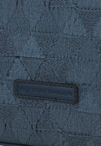 Sac en tissu texturé bleu avec un motif géométrique, portant une étiquette en cuir noir embossée avec "TOM TAILOR."