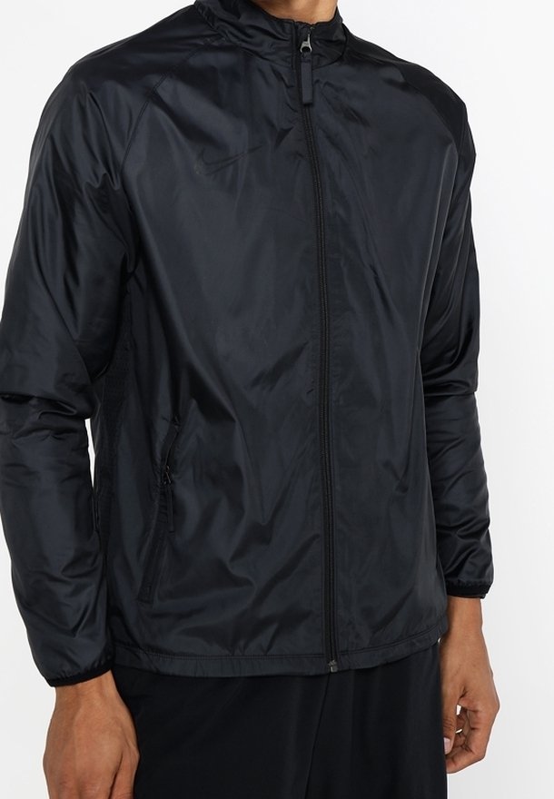 Homme portant une veste noire unie à fermeture éclair avec col montant et manches longues, debout devant un fond blanc.