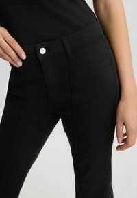 Jeans neri in denim con un design aderente, caratterizzati da una texture liscia, chiusura con bottone argentato e dettagli di cucitura discreti sulle tasche.