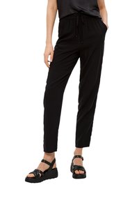 Zwarte, lichte broek met een elastische tailleband en een verstelbaar trekkoord. Gecombineerd met zwarte sandaaltjes met bandjes en een sleehak.
