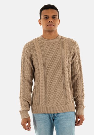 Beige gebreide trui met kabelpatroon, ronde halslijn, geribbelde manchetten en zoom. Draag je over lichtblauwe jeans.