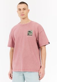 Roze katoenen T-shirt met een ontspannen pasvorm, voorzien van een klein grafisch patch en korte mouwen. Zachte textuur en gestikte zoomdetails.