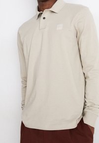 Beige longsleeve poloshirt met een kraag en twee zwarte knopen. Voorzien van een klein logo-op-label op de borst. Zachte, gladde textuur.