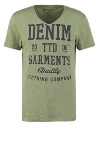 Olivově zelené tričko s krátkým rukávem a výstřihem do V. Na něm je tmavě modrý potisk s texty: "DENIM," "TTD 2006," a "Quality Clothing Company." Hladká textura.