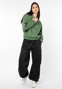 Green sweatshirt with a relaxed fit and ribbed cuffs, paired with black cargo pants featuring large pockets, completed with white sneakers.