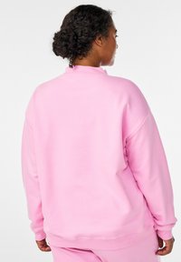 Ružová mikina s dlhými rukávmi a vysokým golierom. Mäkka textúra, voľný strih a rebrované manžety. Žiadne znateľné vzory ani akcenty.