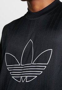 T-shirt de sport noir à col ras du cou haut, avec un design de logo linéaire blanc et de subtiles rayures verticales sur le tissu.