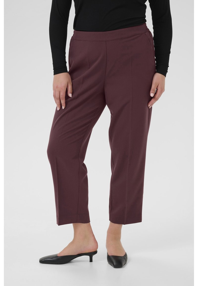 Pantalons sur mesure bordeaux avec une texture lisse, longueur raccourcie, taille élastique et poches latérales, associés à des talons ouverts noirs.