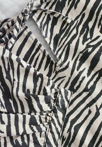 Sort og beige stof med zebra-stribe mønster og en struktureret overflade. Inkluderer en bundet detalje og indsatte taljeaccenter.