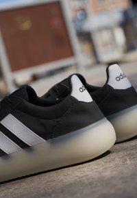 Scarpe da ginnastica Adidas in bianco e nero con suole spesse traslucide posate su una superficie di cemento all'aperto.