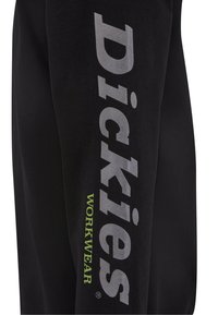 Mustat collegehousut, joissa on suuri "Dickies"-logo harmaana sivulla ja "WORKWEAR" vihreänä. Valmistettu pehmeästä, kestävästä materiaalista.