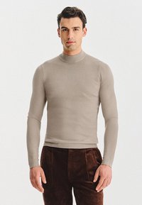 Beżowy długi sweter z golfem i długim rękawem, wykonany z gładkiej dzianiny, o dopasowanym kroju, z prążkowanym wykończeniem na kołnierzu i u dołu.