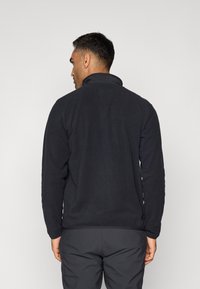 Fleece jacket in solid black, featuring long sleeves, a high collar, and a soft texture. The design includes an elastic hem and cuffs.