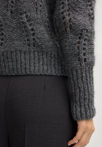 Ciemnoszary sweter w sploty z ribbowym wykończeniem dołu i mankietów, z teksturowanym wzorem oraz ażurowymi detalami wzdłuż rękawów.