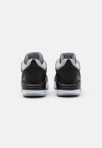 Černé a šedé sportovní boty s texturovanou patou, oranžovým logem a hladkou bílou podešví. Obsahují síťovou podšívku a polstrovaný límec pro pohodlí.