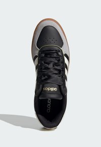 Čierne a šedé tenisky s textúrovaným koženým zvrškom, so třemi bielymi pruhmi a gumovou podrážkou. Majú čierne šnúrky a logo akcenty.