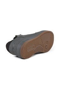 Zapatilla gris con un upper de tela negra texturizada, suela de goma con patrón de espiga y el nombre de la marca en relieve en el costado.