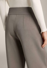 Šedé nohavice s širokými nohavicami a rebrovaným pásom, s hladkou textúrou a jemným prešívaním na zadnej strane pre extra detail.