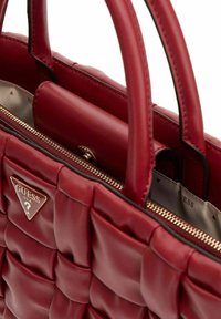 Bolso de mano de cuero rojo con un diseño acolchado, asas dobles y un logo triangular dorado. Bolsillo interior con cremallera y textura suave.