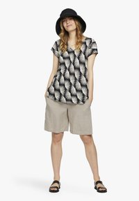 Top de patrón de hojas de palmera en blanco y negro con mangas cortas, combinado con pantalones cortos de lino beige claro y sandalias negras. Accesorios con un sombrero negro.