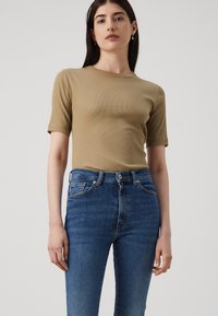 Kaki ribbet t-skjorte med korte ermer, sammen med høytlivede blå denimjeans. Jeansene har en klassisk fem-lomme-design og lite slitasje.